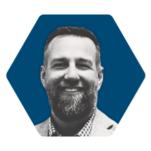 a professional headshot of DC Norris North America Sales Engineer, Brian Irwin. Brian is smiling. The photo of Brian is stylized in black and white and the background is a navy blue hexagon.