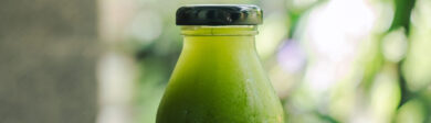 Chilled green soup ready to drink from a glass bottle with a black top