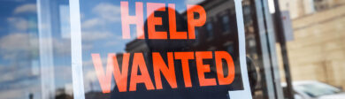 help wanted sign hangs in the window of an office