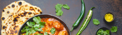 thai curry in a cast iron serving dish with naan and jalapeno pepppers